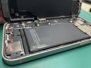 新しいバッテリーの1.5倍程度に膨らんだ危険なバッテリーを慎重に取り外しているiPhone13
