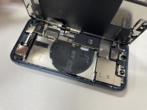 iPhone13miniの内部を開き、水濡れ反応がないことを確認しながら古いバッテリーを慎重に取り外す様子