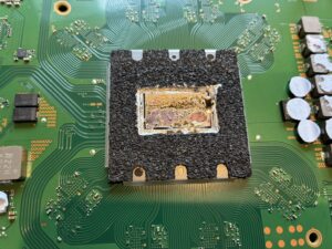 PS5の緑色の基板上にあるAPU（メインチップ）。周囲を黒いスポンジで囲まれ、表面の液体金属が劣化してムラになっている状態。